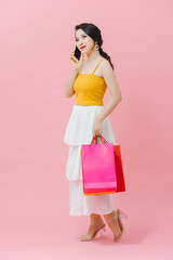 Portrait of a pretty happy girl talking on mobile phone while holding shopping bags over pink background