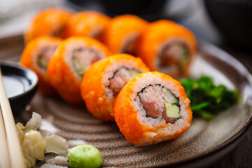 Sushi maki rolls California Futomaki with salmon, avocado, cucumber, crab and flying fish roe on a plate with chopsticks, soy sauce, wasabi and ginger. Japanese traditional seafood served restaurant