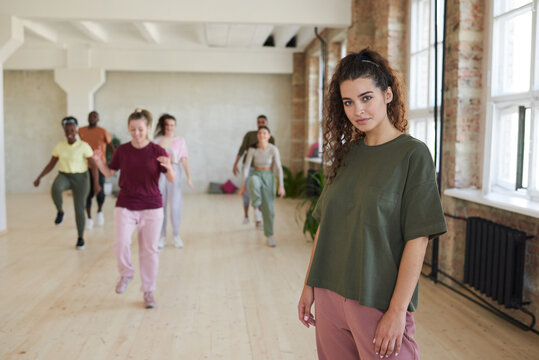 Portrait of young woman in sports clothing looking at camera standing in sport hall with people training in the background