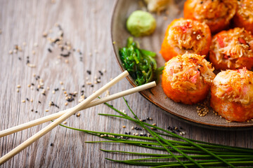 Baked sushi maki rolls with salmon, crab, cucumber, avocado, flying fish roe and spicy sauce on a plate with chopsticks, soy sauce, wasabi and ginger. Japanese seafood served for lunch in restaurant