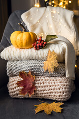Still life in vintage style. Home interior. Knitted clothes are stacked on a gray chair. Home holiday concept on a cold autumn day. Lights, leaves, pumpkin.