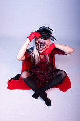 Beautiful funny young woman wearing sugar skull makeup and hat dressed as a witch for Halloween or Dia de Muertos (Day of the Dead); sitting on white background