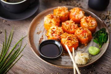 Baked sushi maki rolls with salmon, crab, cucumber, avocado, flying fish roe and spicy sauce on a plate with chopsticks, soy sauce, wasabi and ginger. Japanese seafood served for lunch in restaurant
