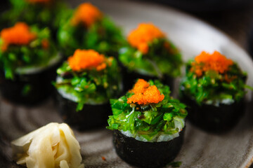 Sushi maki rolls with crab, seaweed salad and flying fish roe on a plate with chopsticks, soy sauce, wasabi and ginger. Japanese traditional seafood served for lunch in modern gourmet restaurant