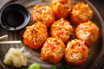 Baked sushi maki rolls with salmon, crab, cucumber, avocado, flying fish roe and spicy sauce on a plate with chopsticks, soy sauce, wasabi and ginger. Japanese seafood served for lunch in restaurant