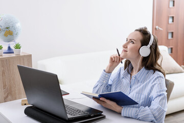 woman in blue shirt listens to music at Desk at home, dreaming, remote work