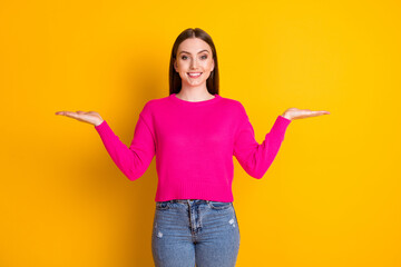 Photo of pretty girl hold two hands empty space beaming smile wear pink pullover isolated yellow color background