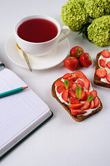 Fototapeta na wymiar morning tea, still life, Notepad with pencil, tea with hibiscus, sandwich with strawberries and cottage cheese, flowers on white background