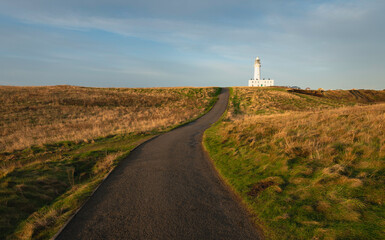 Lighthouse under blue sky with grasses and road in foreground, Flamborough, UK.