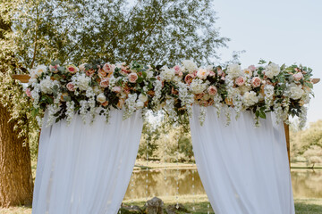 Wedding ceremony outdoors in the park. White arch decorated with roses.