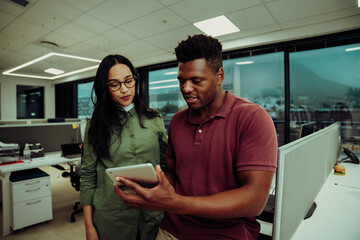 Multi-ethnic partners submitting business report using digital tablet standing in office block