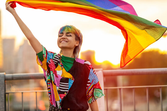 Portrait of happy non-binary person waving rainbow flag
