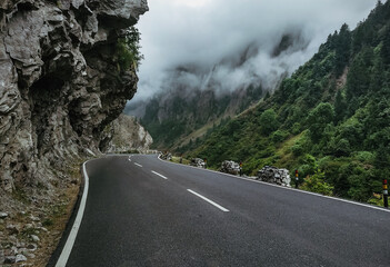 An empty road with green mountains and clouds by the side