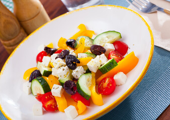 Fresh colorful Greek salad (horiatiki salad) served with feta cheese on white plate..
