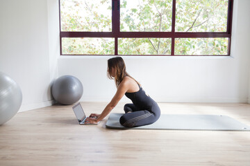 Naklejka na ściany i meble sporty woman in sportswear sitting on the floor using laptop at home