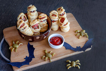 mummy sausages lies on a cutting board with ketchup and olive spiders