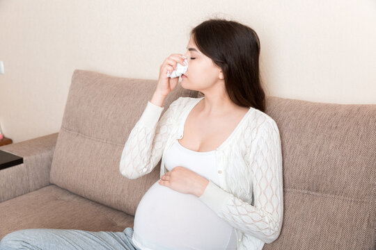 Sick pregnant woman blowing nose into tissue at home Healthy millennial healthcare concept