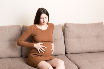 Pregnant Lady Having Massaging Lower belly Sitting On Sofa Indoor. Pregnancy Problems Concept. Maternity healthcare