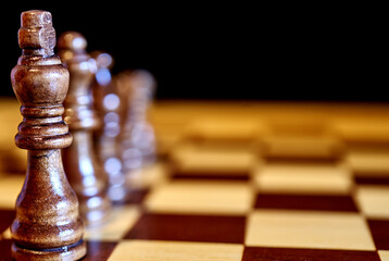 Chess concept, row of black pieces with the king in front, selective focus, intentionally small...
