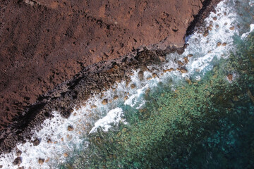 Aerial top view of waves splashing on rocky volcanic coastline. High quality photo