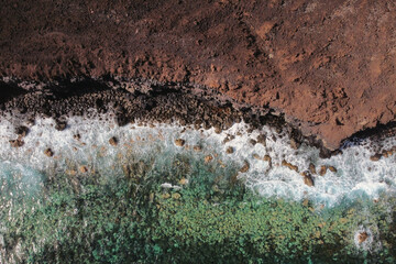 Aerial top view of waves splashing on rocky volcanic coastline. High quality photo