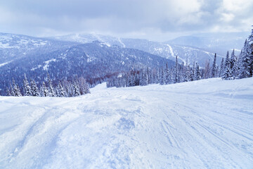 View of ski resort Sheregesh from Utya mountain. Snowdrifts and snow-covered trees in fluffy snow, sky in clouds, winter landscape, cold weather.