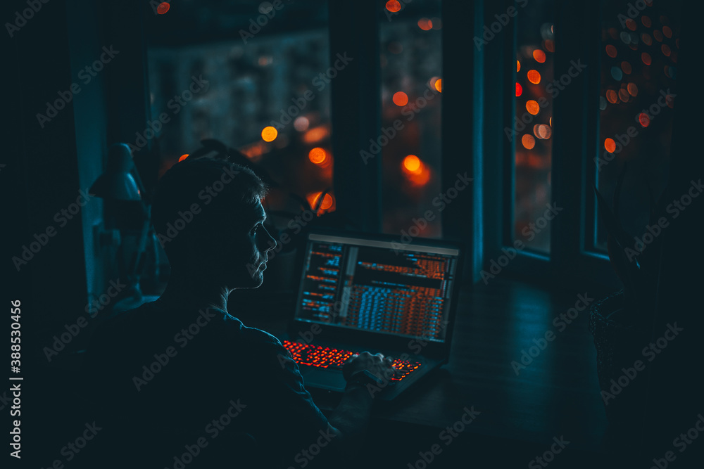 Wall mural a young man programmer coding on a laptop in the dark with a view of the lights of the night city, c