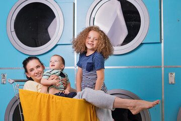 Mother Household With Children Wearing Pyjamas Having Fun And Doing Laundry At Self Service...