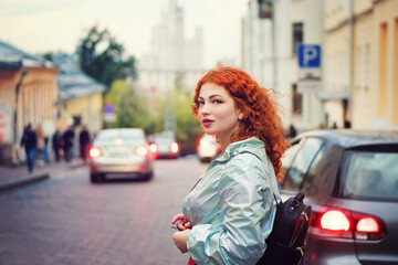 Fototapeta premium Romantic Curly Red-haired Girl Walking Through Town At Evening