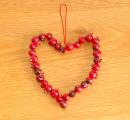 Obraz premium Hanging Christmas tree decoration red berries in heart shape on wood background