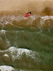 Aerial top down view of red fishing boat anchored on sand beach near sea waves. Nautical vessel, water transport. Minimalism art nature photography.