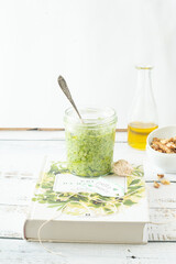 Arugula Chive Basil Pesto served in a glass jar with nuts . Photographed from front view on a black/light blue background.