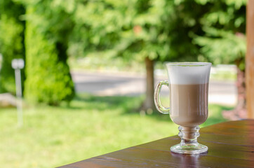 Glass cup of latte coffee on the wooden table outdoors.