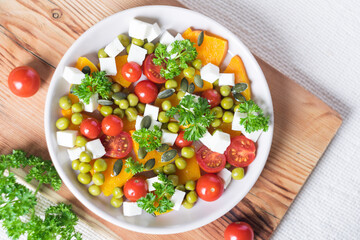 Mixed salad with pumpkin, parsley, tomatoes and feta cheese, healthy food for diet. Top view, close-up