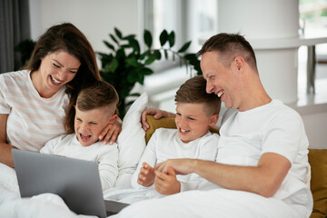 Obraz premium Beautiful parents with kids enjoying at home. Young family watching movie on lap top..