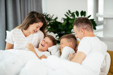 Fototapeta premium Young family enjoying in bed. Happy parents with sons relaxing in bed.
