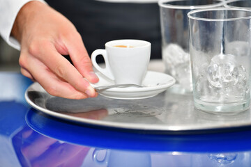 Close up of male hand holding a cup of coffee over a bar tray with glasses on it. Bartending and coffee concept.