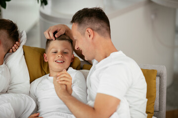 Father and son enjoying in bed. Happy man with son relaxing in bed..