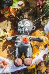 voodoo doll pierced by needles lies on a table with fallen leaves and pumpkins