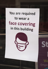 Don't make us wear a mask, you are required to wear face covering sign on a shop window trying to follow social distancing guidance and government guidelines to avoid forced closure from COVID-19