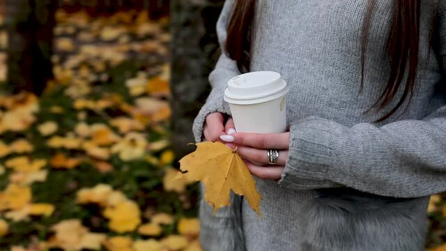 Girl holding a cup of coffee with her. Moving camera takes pictures. Autumn season in the park.