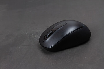 Black wireless mouse on gray background, dark tone.