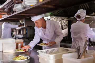 Confident experienced chef in white uniform working in professional kitchen of restaurant