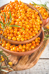 Sea buckthorn berries in small organic wooden bowl, with sea buckthorn branches on white wooden desk background