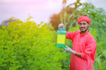 Young indian farmer showing fertilizer bottle at green field
