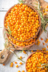 Sea buckthorn berries in small organic wooden bowl, with sea buckthorn branches on white wooden desk background