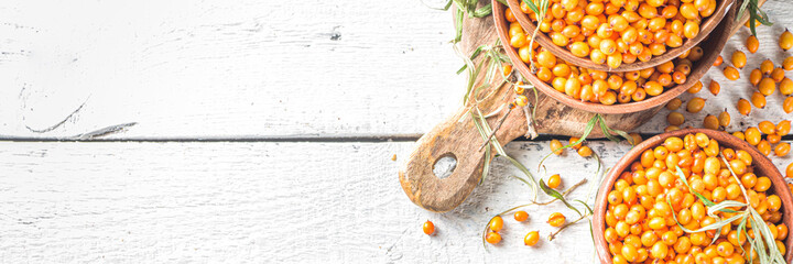 Sea buckthorn berries in small organic wooden bowl, with sea buckthorn branches on white wooden...