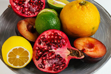 Closeup of a mandarin, lime, lemon, pomegranate and plum on a gray dish isolated on white background.