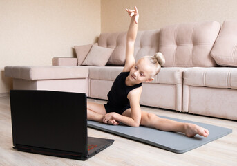 The child watches online video on a laptop and performs sports exercises - yoga, gymnastics. Stay...