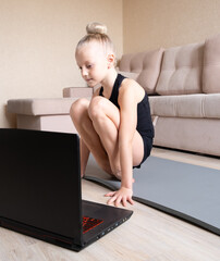 The child watches online video on a laptop and performs sports exercises - yoga, gymnastics. Stay at home. Self-isolation, quarantine, online education concept.